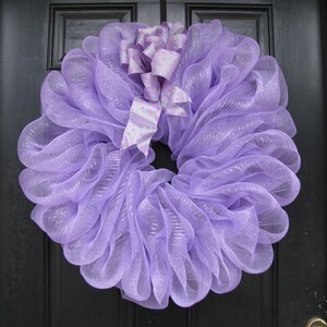 May include: A lavender wreath with a pink and green polka dot bow. The wreath is made of mesh and is perfect for a spring or summer door decoration.