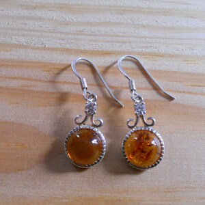 May include: A pair of silver dangle earrings with amber stones and clear crystal accents.