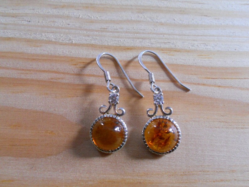 May include: A pair of silver dangle earrings with amber stones and clear crystal accents.