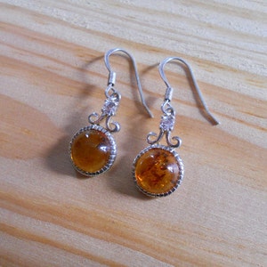 May include: A pair of silver earrings with amber stones and clear crystal accents. The earrings have a delicate, ornate design.
