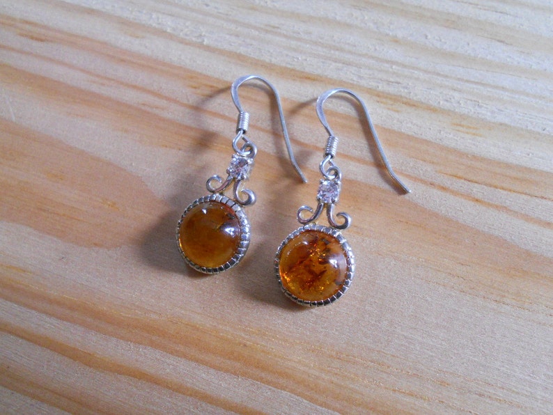 May include: A pair of silver earrings with amber stones and clear crystal accents. The earrings have a delicate, ornate design.