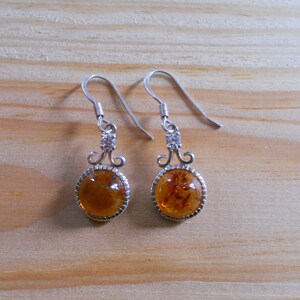 May include: A pair of silver dangle earrings with amber stones and clear crystal accents.