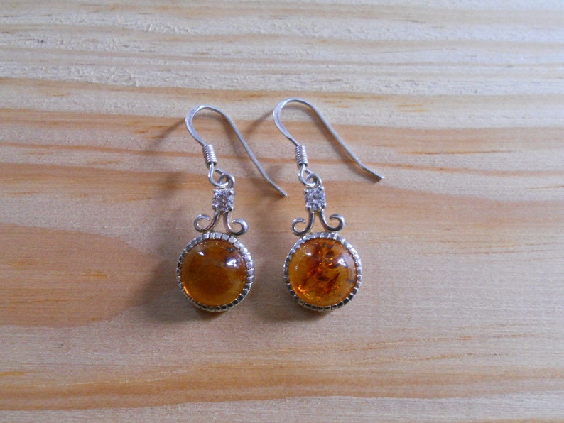 May include: A pair of silver dangle earrings with amber stones and clear crystal accents.