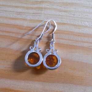 May include: A pair of silver earrings with amber stones. The earrings have a delicate design with a small loop at the top and a round amber stone in the center.