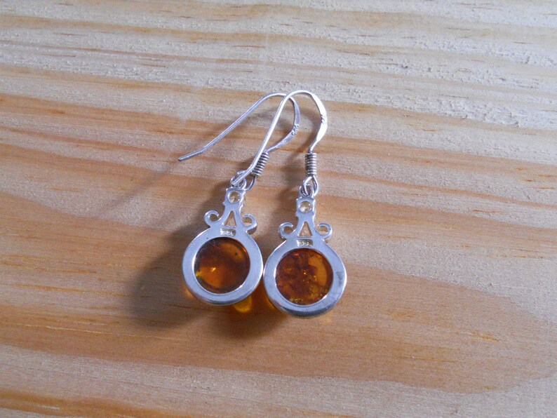 May include: A pair of silver earrings with amber stones. The earrings have a delicate design with a small loop at the top and a round amber stone in the center.