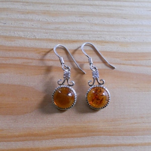 May include: A pair of silver dangle earrings with round amber stones. The earrings have a delicate, ornate design.