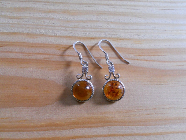 May include: A pair of silver dangle earrings with round amber stones. The earrings have a delicate, ornate design.