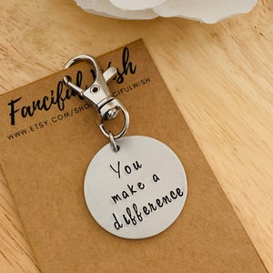 May include: A silver keychain with a round metal tag that says "You make a difference". The keychain is on a brown paper card with the text "Fanciful Wish" and a website address.