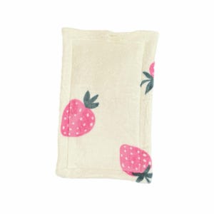 May include: A rectangular, cream-colored plush blanket featuring a repeating pattern of pink strawberries with green leaves. The blanket has a soft, textured appearance and a stitched border.