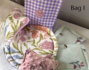May include: A purple and white gingham paper bag labeled Bag 1 with a Thank You sticker, accompanied by a floral patterned circular pad, a pink dinosaur print textured square pad, and two light green square pads with small bee and floral prints.