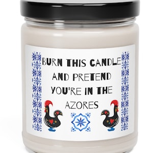 Op de afbeelding: Een witte kaars met een zwarte deksel en een label met de tekst "Burn this candle and pretend you're in the Azores". Het label heeft ook twee hanen en een blauw en wit tegelpatroon.