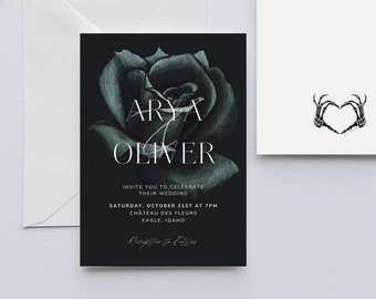 Puede incluir: Un conjunto de invitaciones de boda con un diseño floral oscuro. La tarjeta de invitación tiene los nombres "ARYA OLIVER" en texto blanco, con detalles del evento. También hay una tarjeta a juego con un corazón hecho de manos de esqueleto, junto con un sobre blanco.