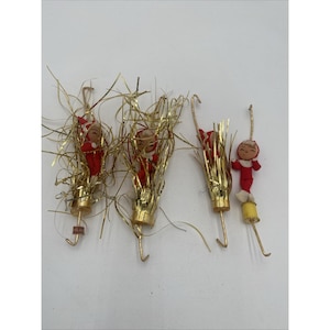 May include: Four vintage Christmas tree decorations. Each features a small doll in a red outfit and white hat, surrounded by gold tinsel. They are attached to gold hooks. One has a yellow base.