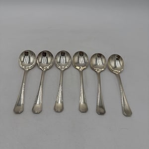 May include: Six silver spoons arranged in a row. Each spoon has a rounded bowl and a long, slender handle with a rectangular end. The spoons are reflective, showing the surrounding environment. The spoons are likely for serving or eating.