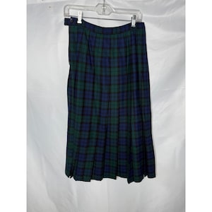May include: A knee-length pleated skirt featuring a dark green and navy blue plaid tartan pattern. The skirt has a high waistband with a single button closure on the side and is displayed hanging from a clear plastic garment hanger.