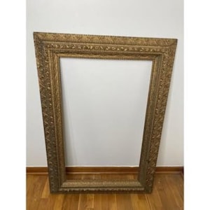 May include: A large, rectangular picture frame with a metallic gold finish. The frame features an ornate, repeating embossed pattern along its wide border, creating a textured appearance. The inner edge is beveled, leading to a hollow center.