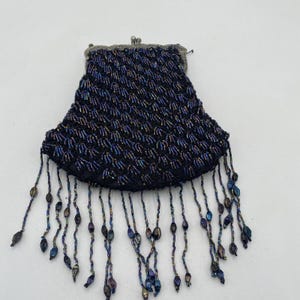 May include: A vintage beaded purse with a silver-toned clasp. The purse is black with a textured pattern and features dangling beaded fringe in shades of blue, purple, and gold. The purse is likely from the early to mid-20th century.