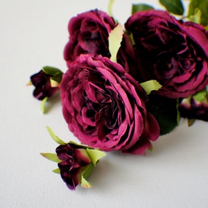 May include: A bouquet of deep burgundy roses with green leaves. The roses are arranged in a cluster with some buds.