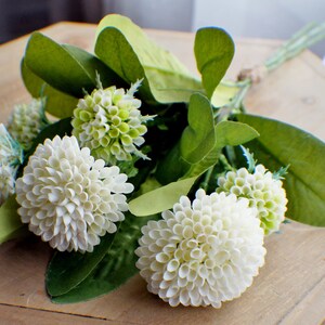 May include: A bouquet of white and green artificial flowers. The flowers are arranged in a cluster and have a delicate, layered appearance. The bouquet is perfect for adding a touch of natural beauty to any space.