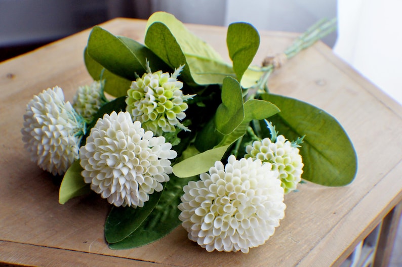 May include: A bouquet of white and green artificial flowers. The flowers are arranged in a cluster and have a delicate, layered appearance. The bouquet is perfect for adding a touch of natural beauty to any space.