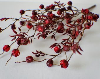 May include: A bunch of artificial red berry sprigs with dark red leaves. The sprigs are arranged in a loose, natural-looking cluster.