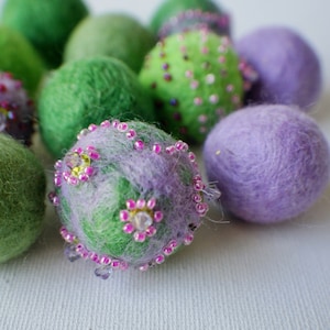 Könnte beinhalten: Eine Gruppe von Filz-Ostereiern in Grün- und Lilatönen, verziert mit rosa und durchsichtigen Perlen. Einige der Eier haben eine flauschige Textur.