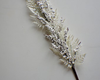 May include: A white artificial sprig with small white berries and delicate white leaves. The sprig is attached to a brown stem.