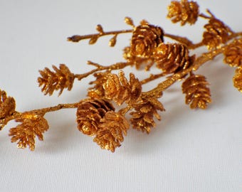 May include: A gold glitter pine cone garland with a branch and multiple pine cones. The pine cones are clustered together and have a shiny, sparkly finish.