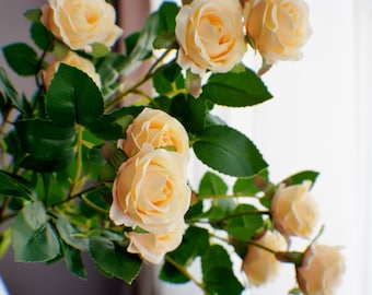 May include: A bouquet of artificial peach-colored roses with green leaves. The roses are arranged in a vase.