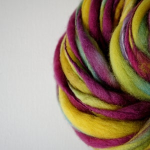 May include: A close-up of a vibrant skein of hand-dyed yarn. The yarn features a blend of colors, including yellow, purple, green, and teal. The wool is thick and textured, ideal for knitting or other fiber crafts.