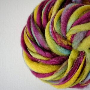 May include: A close-up of a vibrant ball of hand-dyed yarn. The yarn is a mix of colors, including yellow, magenta, light green, and blue. The yarn is thick and textured, perfect for knitting or crocheting projects.