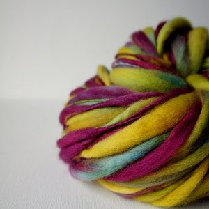May include: A vibrant ball of yarn in shades of yellow, magenta, and teal. The thick, textured yarn is tightly wound, creating a visually appealing and tactile product. Ideal for knitting or crochet projects.