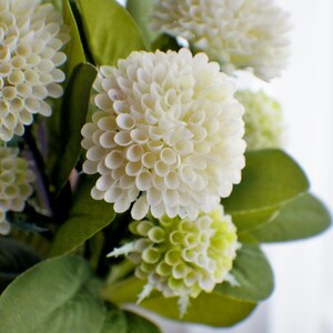 May include: A bouquet of white and green artificial flowers with green leaves. The flowers are arranged in a vase.