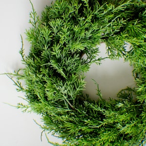 Könnte beinhalten: Ein grüner Kranz aus Zedernzweigen. Der Kranz ist rund und hat einen Durchmesser von etwa 30 cm.