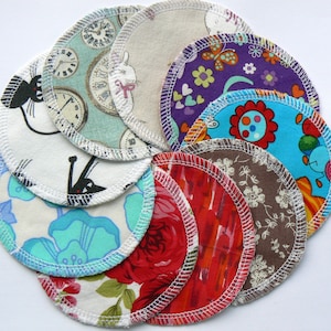 May include: A selection of circular fabric pads with white stitched edges. The pads display diverse, colourful patterns such as floral, clocks, cats, and abstract designs. The pads are arranged in a circular formation, highlighting the range of prints.