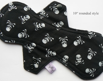 May include: A black reusable sanitary pad with a white skull and crossbones pattern. The pad is approximately 10 inches long and has a rounded style. It features snap closures and a small label that reads "zillys".