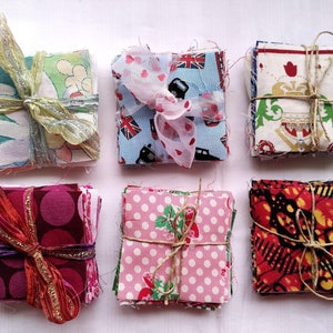 May include: Six stacks of fabric squares, each tied with twine or ribbon. The fabric squares are in various patterns and colours, including pink, red, blue, green, and white.
