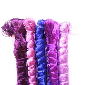 May include: Five spools of thread in shades of purple, pink, and blue. The thread is wound tightly and the ends are frayed.