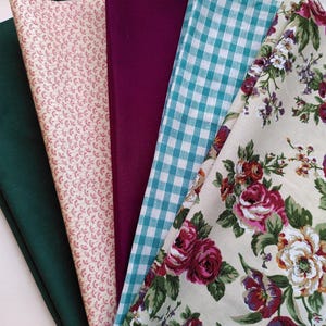 May include: A selection of fabric samples in diverse patterns and colours. Features solid green, pink floral, solid purple, teal gingham, and a cream floral print with red and purple roses.