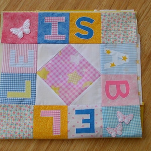 May include: A colorful patchwork quilt with the word "BELIEVE" spelled out in white letters on a pink, blue, and yellow background. The quilt is decorated with butterflies and stars.