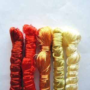 May include: Four spools of thread in different colours: red, orange, yellow, and white. The thread is wound tightly and is ready for use in sewing or embroidery.