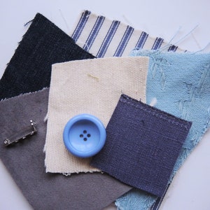 May include: Assortment of fabric swatches in various shades of blue, grey, and white, including a striped pattern and a textured fabric. A blue button and a silver metal pin are also included.