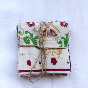 May include: A stack of fabric squares with a white background and a gold, green, and red floral pattern. The fabric is tied together with twine.