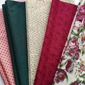 May include: A selection of fabric swatches in diverse patterns and colours. The fabrics include a pink dotted pattern, solid dark green, a cream-coloured pattern, a red paisley design, and a floral print with pink and purple roses.