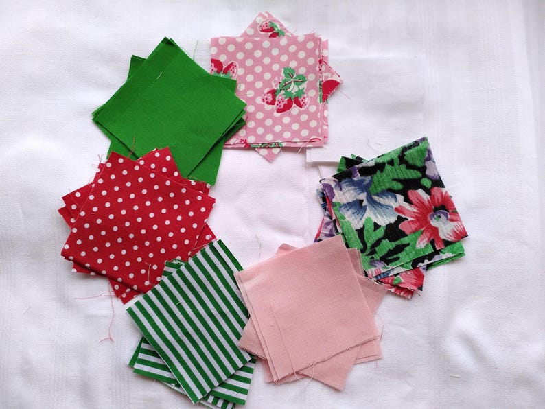 May include: A collection of fabric squares in various patterns and colors, including green, pink, red, and floral. The squares are arranged in a circle on a white surface.