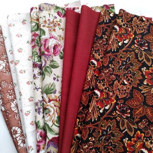 May include: A selection of fabric swatches featuring diverse patterns. The fabrics include a brown floral print, a white dotted fabric, a floral print with pink roses, a solid red fabric, and a dark floral print with brown and orange details.
