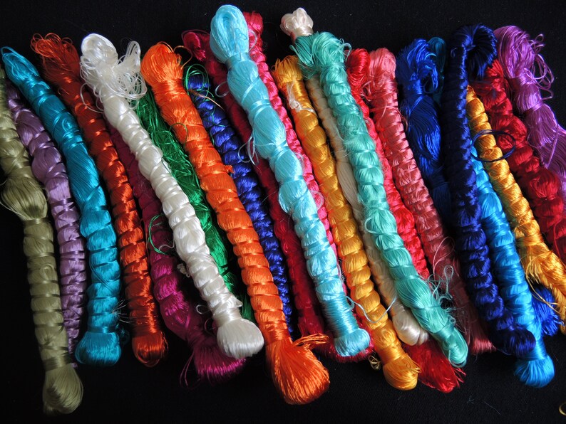 Puede incluir: Una colecci&oacute;n de hilos trenzados de colores en varios tonos de azul, verde, rojo, naranja, morado y blanco. Los hilos est&aacute;n dispuestos en una fila y todos tienen aproximadamente la misma longitud.