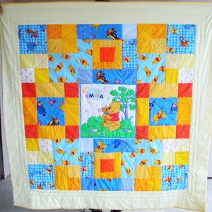 Könnte beinhalten: Eine gelbe, blaue und rote Patchwork-Decke mit einem Winnie Puuh und Ferkel-Motiv in der Mitte. Die Decke ist mit dem Namen "Emma" personalisiert.