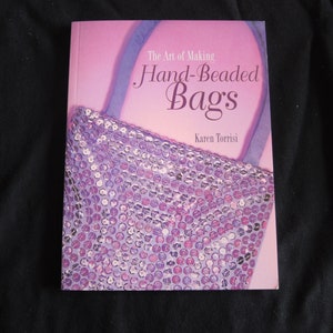 May include: The Art of Making Hand-Beaded Bags book cover featuring a purple sequined handbag with a blue strap.