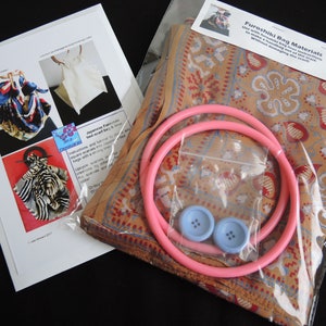 May include: A kit for making a Japanese Furoshiki bag. It includes a printed fabric square, two pink plastic rings, and two blue buttons. The instructions say "Use with a reusable bag instructions to make a handbag out of the scarf without damaging the scarf."